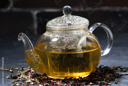 fresh tea in a glass teapot on dark background, closeup