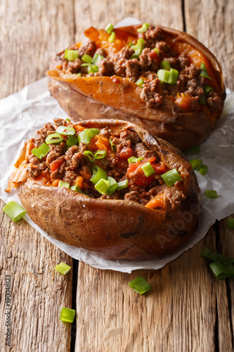 Delicious baked sweet potato stuffed with ground beef and green onion close-up on paper on the table. vertical