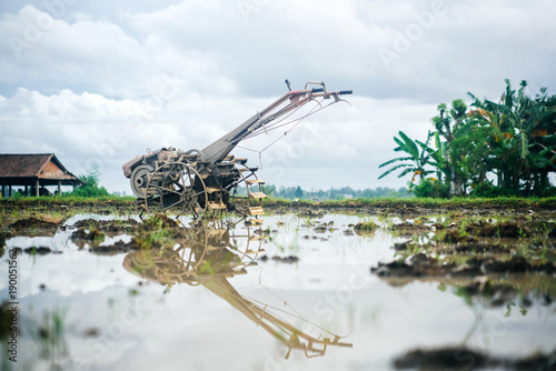 old mini combine harvester machine on a rice field in the evening with a reflection in the water.