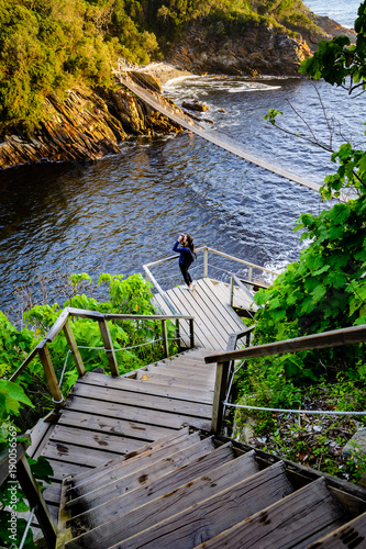 A woman looking through binoculars on a flight of stairs leading to the suspension bridge in Storms River Mouth national park in South Africa