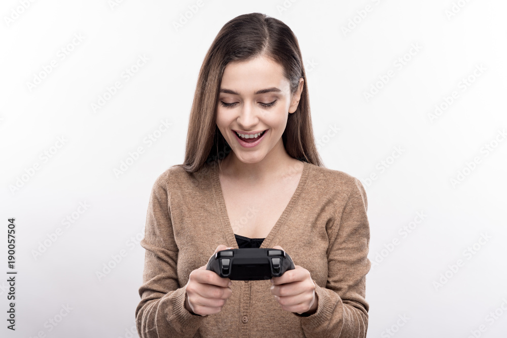 Excited about purchase. Charming young woman holding a new video game controller and looking at it with smile while posing isolated on a white background