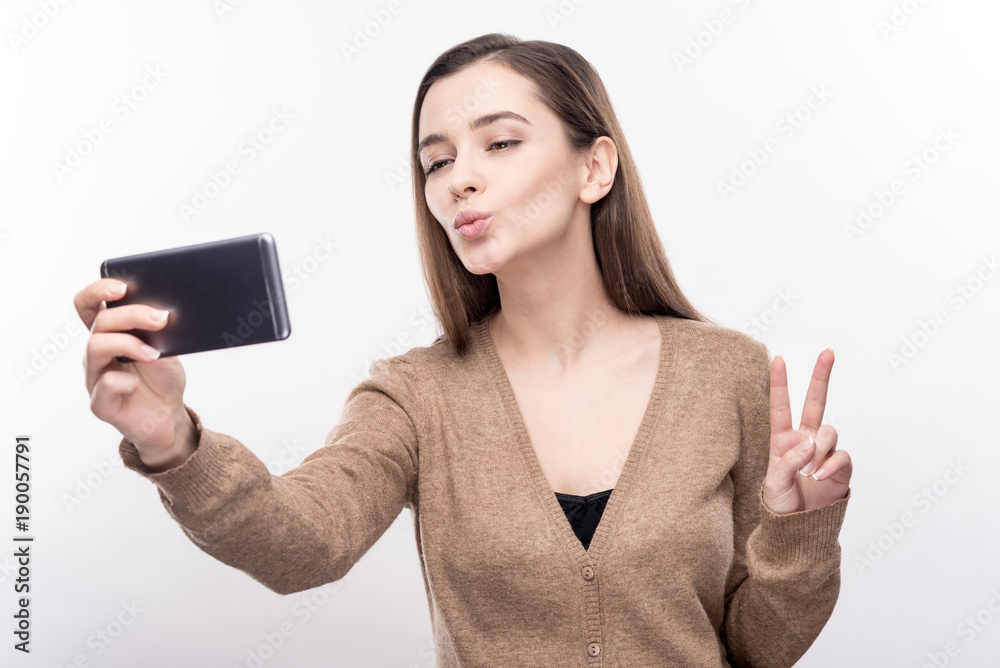 Loving myself. Adorable young woman showing a V sign and taking selfies while posing isolated on a white background Loving myself. Adorable young woman showing a V sign and taking selfies while posing isolated on a white background