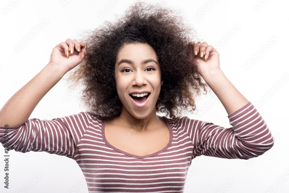 Adorable hairstyle. Charming cute young woman in a striped pullover touching her curly hair and smiling for the camera cheerfully Adorable hairstyle. Charming cute young woman in a striped pullover touching her curly hair and smiling for the camera cheerfully