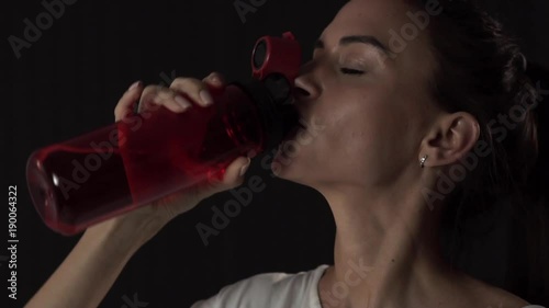 Slim young woman drinking water after training slow motion photo