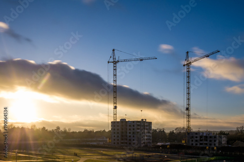 Tower cranes and unfinished multi-storey high near buildings under construction site in the sunset evening with dramatic colorful cloud background