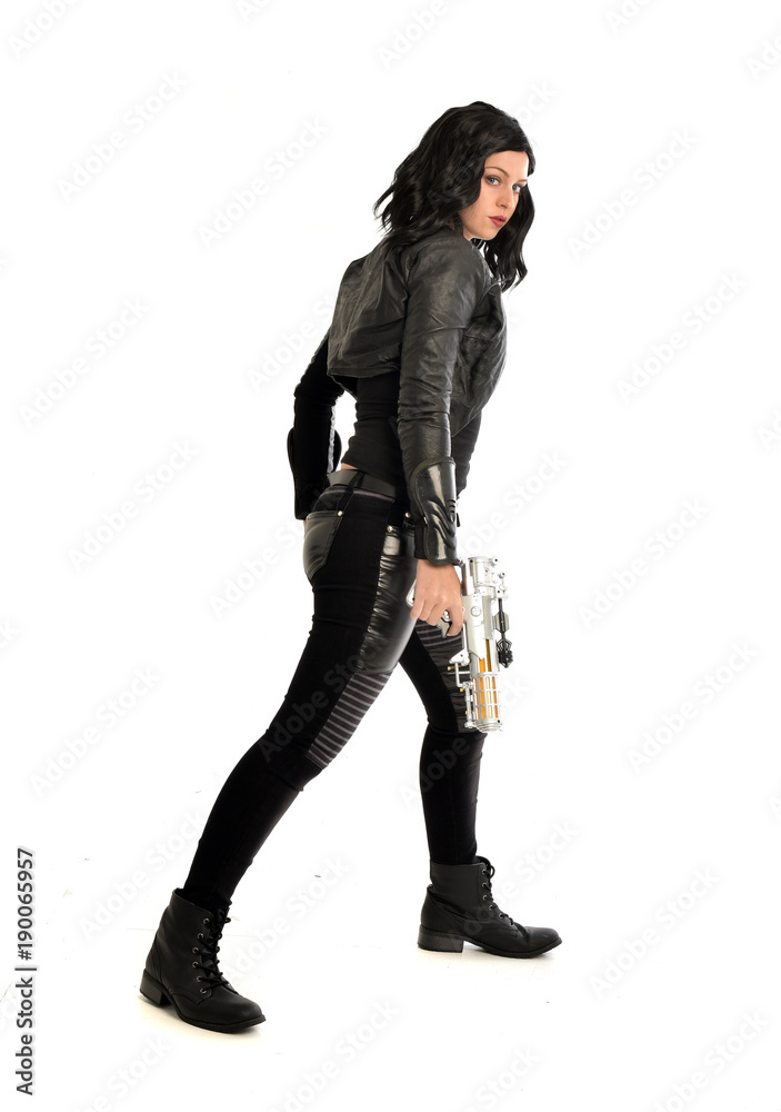 full length portrait of black haired girl wearing leather outfit. standing pose while holding a gun, isolated on a white studio background. full length portrait of black haired girl wearing leather outfit. standing pose while holding a gun, isolated on a white studio background.