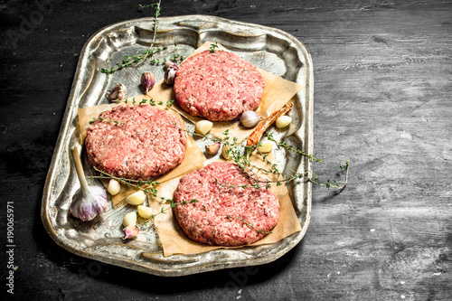 Raw burger with garlic and spices on a steel tray.