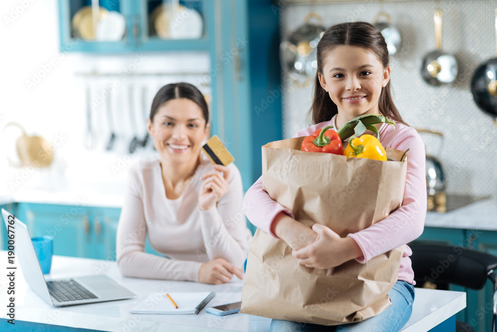 Online shopping. Beautiful cheerful dark-haired girl and mother smiling and the girl holding a packet and mom holding a card