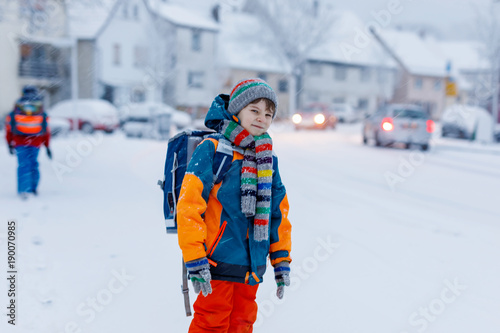 Two little kids boys of elementary class walking to school during snowfall