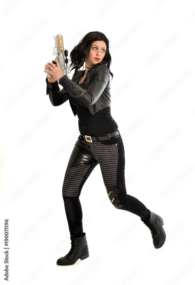 full length portrait of black haired girl wearing leather outfit. standing pose while holding a gun, isolated on a white studio background. full length portrait of black haired girl wearing leather outfit. standing pose while holding a gun, isolated on a white studio background.