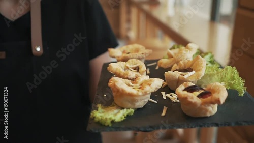 Waiter is bringing out food to the customer. Gourmet appetizer with green lettuce salad leaf, grated cheese. Delicious food on dark background.