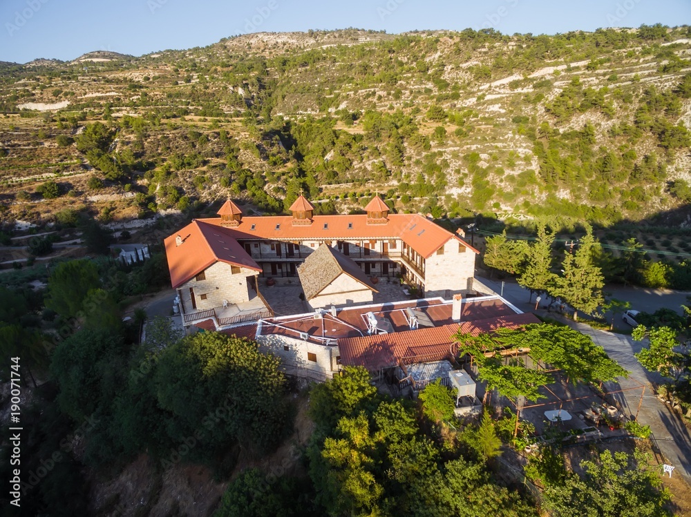 Aerial bird's eye view of christian greek orthodox Holy Monastery of Panayia Amasgous in Monagri village,Limassol,Cyprus. The traditional stone ceramic roof tiled church in the forest slope from above