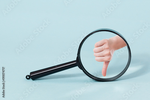 Hand with thumb down throw Magnifying glass, on a pastel blue background