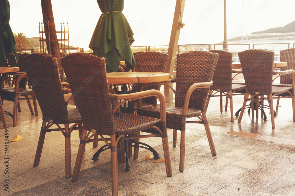 Empty open cafe on the coast - tables and wicker chairs stand on the background of the sea on sunny day