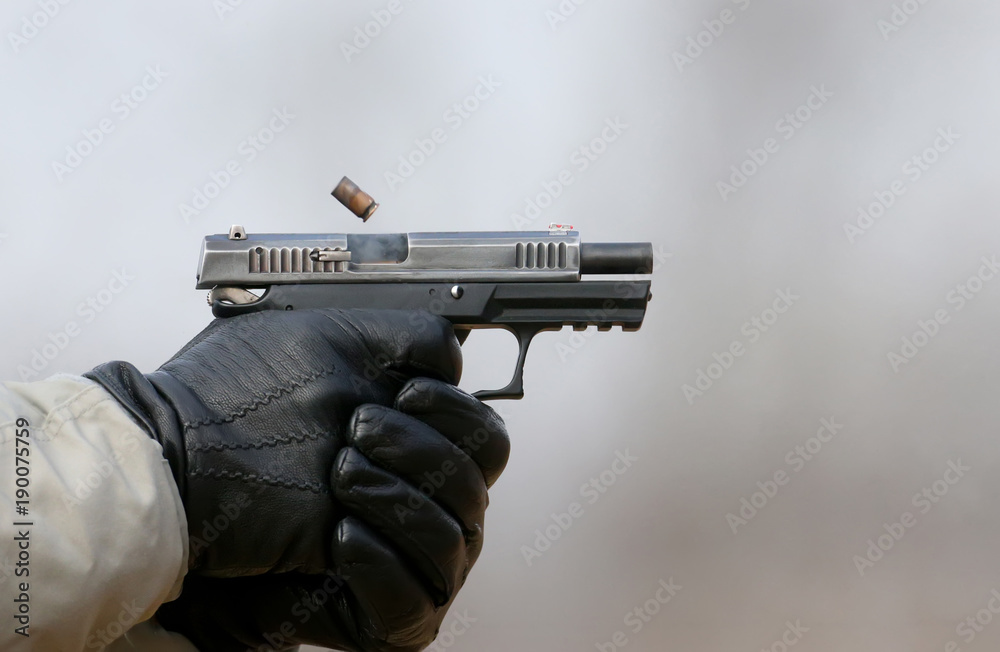 Close-up Photo of a pistol shooting with two hands, the shells emanating from the shutter and blue smoke on a blurred background. Close-up Photo of a pistol shooting with two hands, the shells emanating from the shutter and blue smoke on a blurred background.