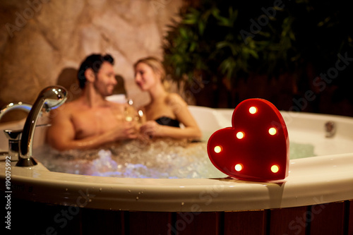 Heart on a background of a romantic couple with champagne in the jacuzzi. Valentines day.
