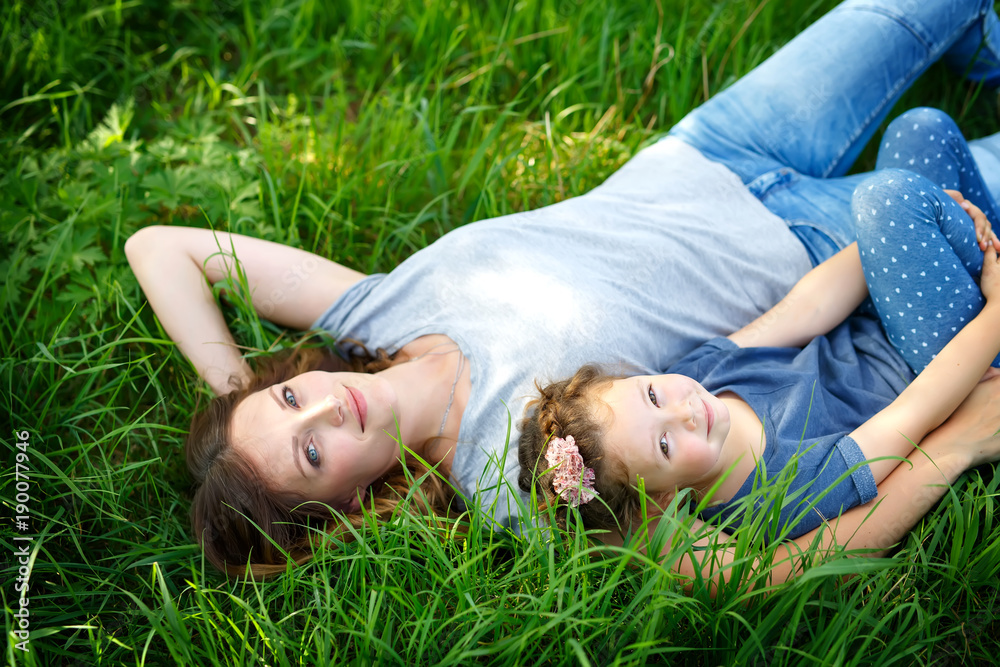 Beautiful young mother and little daughter lying on green grass and resting Beautiful young mother and little daughter lying on green grass and resting