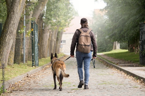Femme avec un malinois. Post apocalypse. voyager à pied avec son chien. Femme qui marche sur un chemin de pierre avec un sac à dos.Femme qui se dirige vers le bâtiment au bout de la route.