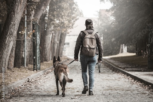 Femme avec un malinois. Post apocalypse. voyager à pied avec son chien. Femme qui marche sur un chemin de pierre avec un sac à dos.Femme qui se dirige vers le bâtiment au bout de la route.