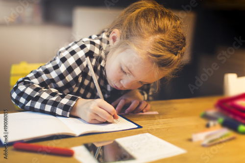 beautiful, blond girl is sitting at the table and is doing schoolwork at home photo