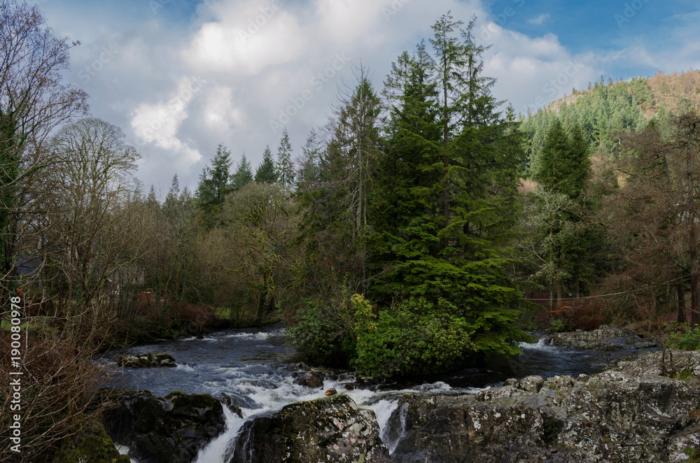 Beautiful river scene with trees on a small island and a waterfall in the foreground at the village of Betws Y Coed in North Wales