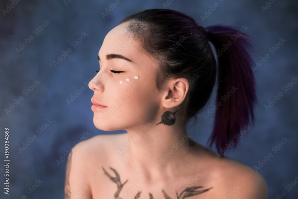Beautiful girl with dyed hair and tattooes posing in studio on blue background Beautiful girl with dyed hair and tattooes posing in studio on blue background