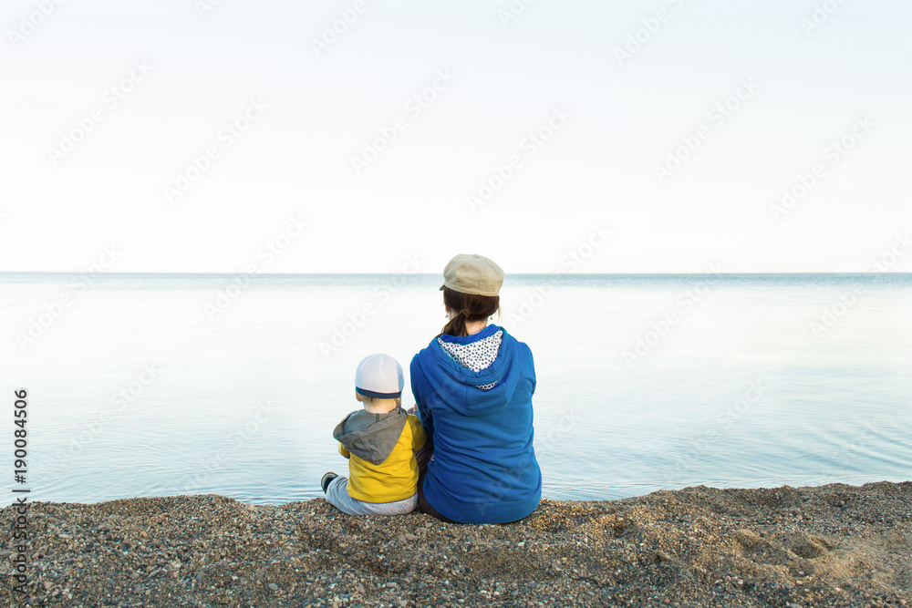 Mother or sister with child looking at sea far away and sitting on shore Mother or sister with child looking at sea far away and sitting on shore