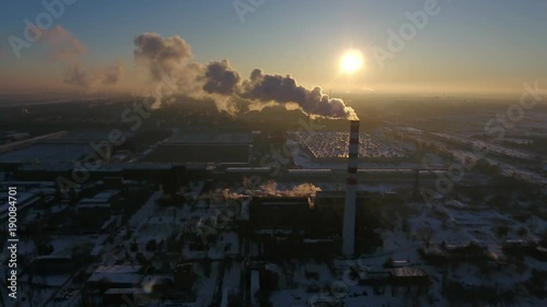 A bird`s eye view of a huge boiler chimney with a white smoke flow at a splendid  sunset in winter. The cityscape is urban and fine photo