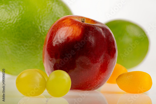 Intensywnie kolorowe i okrągłe - czerwone jabłko z innymi owocami na białym tle