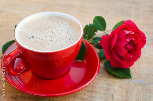 Red cup of morning coffee or cappuccino and rose.
