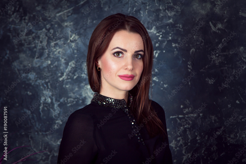 Portrait of beautiful young smiling brunette woman, wearing black blouse, standing behind dark grey background Portrait of beautiful young smiling brunette woman, wearing black blouse, standing behind dark grey background
