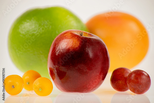 Intensywnie kolorowe i okrągłe - czerwone jabłko z innymi owocami na białym tle