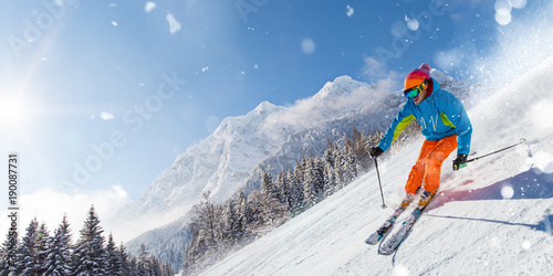 Skier on piste running downhill in beautiful Alpine landscape. Blue sky on background.