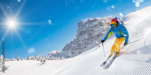 Skier on piste running downhill in beautiful Alpine landscape. Blue sky on background.