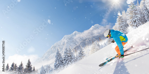 Skier on piste running downhill in beautiful Alpine landscape. Blue sky on background.