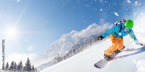 Snowboarder on piste running downhill in beautiful Alpine landscape. Blue sky on background.