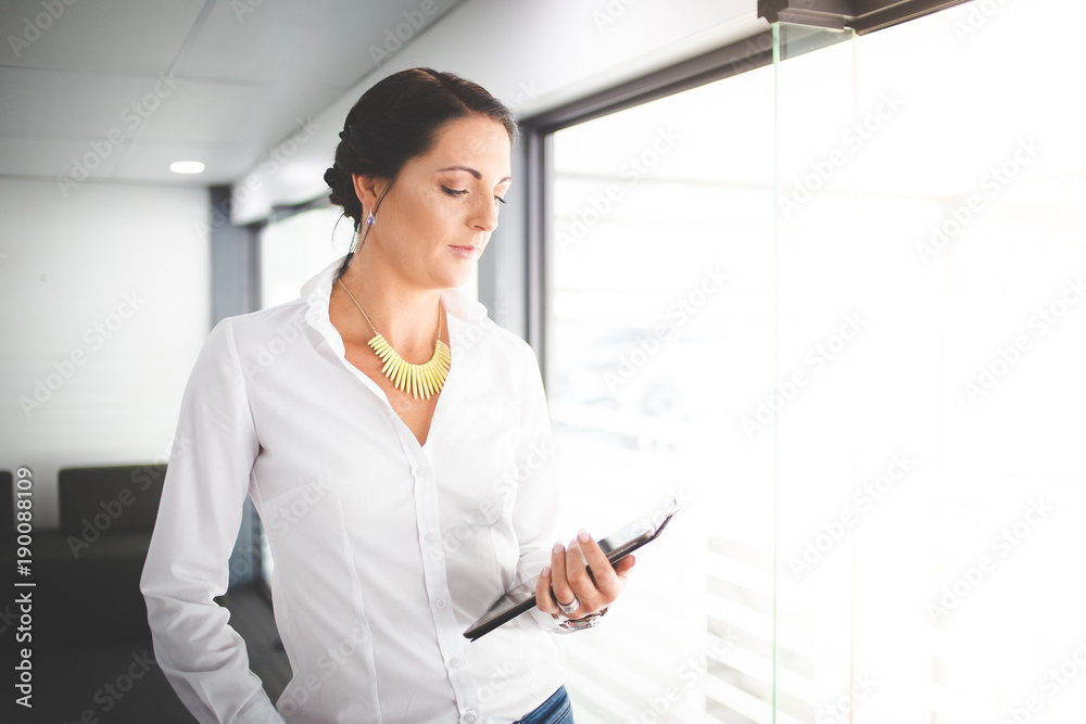 Beautiful brunette business woman standing in a boardroom working on a tablet computer Beautiful brunette business woman standing in a boardroom working on a tablet computer