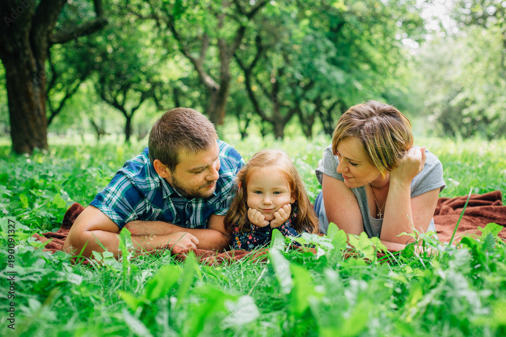 Young happy family of three lying on blanket in the park having fun. Happy parenting concept. Little girl with mother and father outdoors Young happy family of three lying on blanket in the park having fun. Happy parenting concept. Little girl with mother and father outdoors