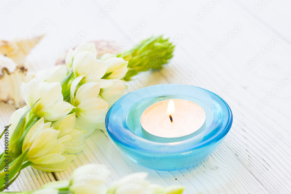 Aromatherapy Spa Concept with a fragrant candle in a blue glass candle holder, and beautiful white flower on white wooden background, close up Aromatherapy Spa Concept with a fragrant candle in a blue glass candle holder, and beautiful white flower on white wooden background, close up