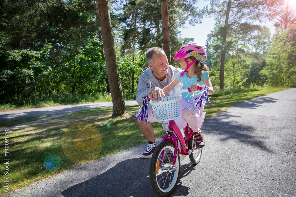 Father teaching his daughter to ride bicycle. Happy kid learning riding bike. Family spending time together. Sunny summer day on suburb street. Father teaching his daughter to ride bicycle. Happy kid learning riding bike. Family spending time together. Sunny summer day on suburb street.