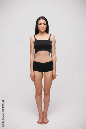 serious young brunette woman in black underwear standing on gray studio background. full length photo