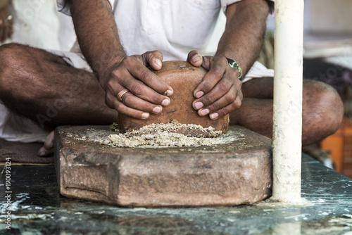 Thandai seller preparing / grinding thandai masala made of cardamom,saffron, almonds fennel seeds with hands on wooden base in Nathdwara, Rajasthan, India