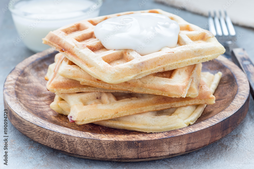 Homemade savory belgian waffles with bacon and shredded cheese, served with plain yogurt, on wooden plate, horizontal