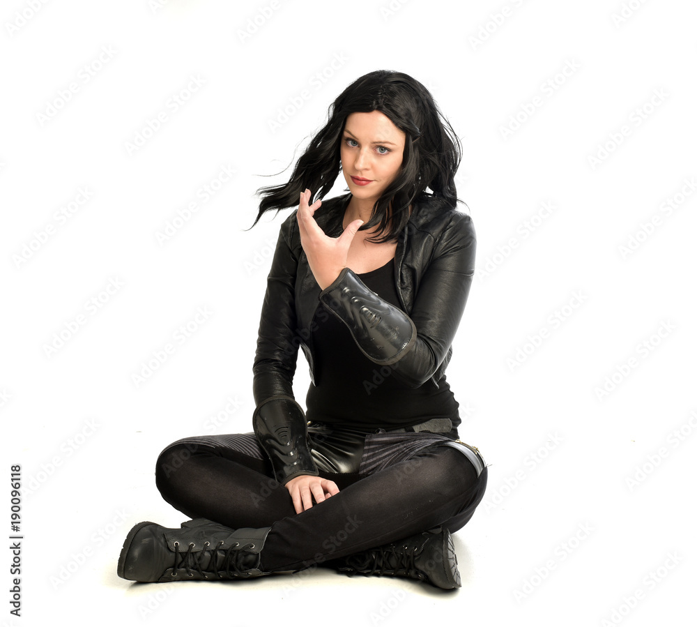 full length portrait of black haired girl wearing leather outfit. sitting pose, isolated on a white studio background. full length portrait of black haired girl wearing leather outfit. sitting pose, isolated on a white studio background.