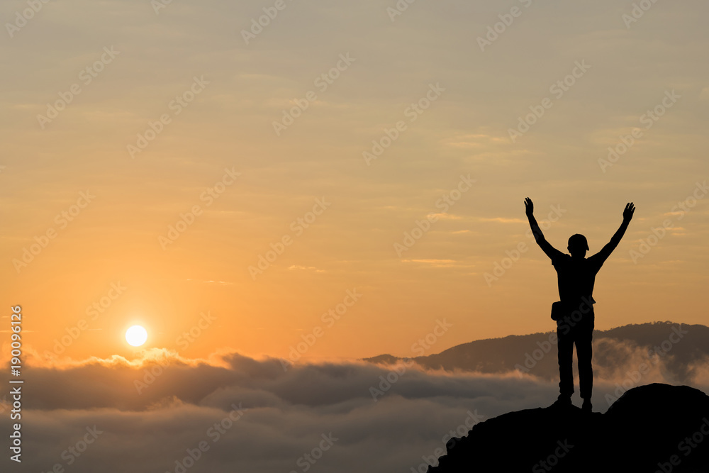 Silhouette of man hold up hands on the peak of mountain.