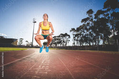 Female fitness model and track athlete sprinting on an athletics track made from tartan