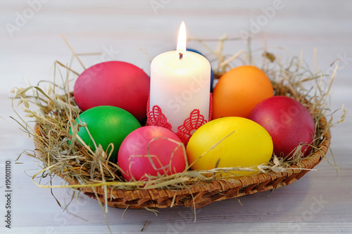 In the wicker basket lie Easter multi-colored eggs and a burning candle.