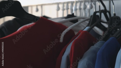 wardrobe hanger with multi-colored clothes in the store. colorful outfits hang on a hanger. a woman's hand takes a hanger with a red dress. pulls out of the closet 4k