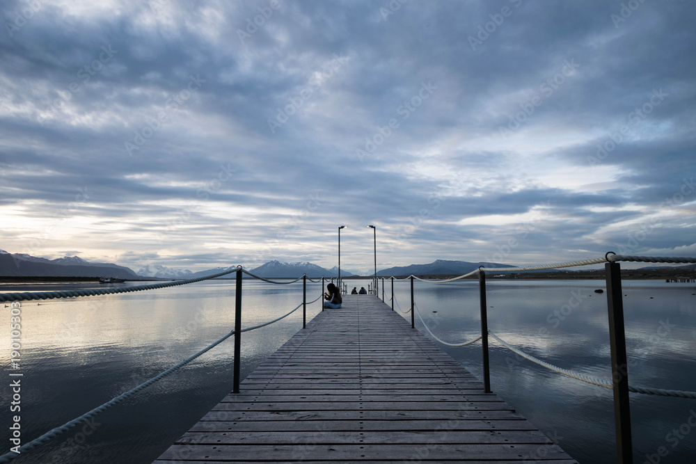 Wood bridge at sunset with calm water and clouds reflections, Puerto Natales, Chile