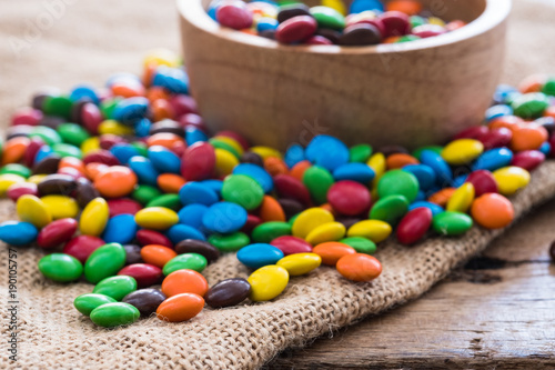 colorful round chocolate candies on gunny sack cloth on wood table, selective focus